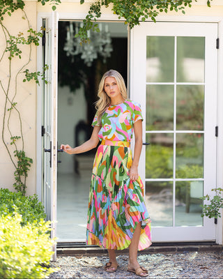 Woman in a colorful dress standing in front of a glass door with greenery around.